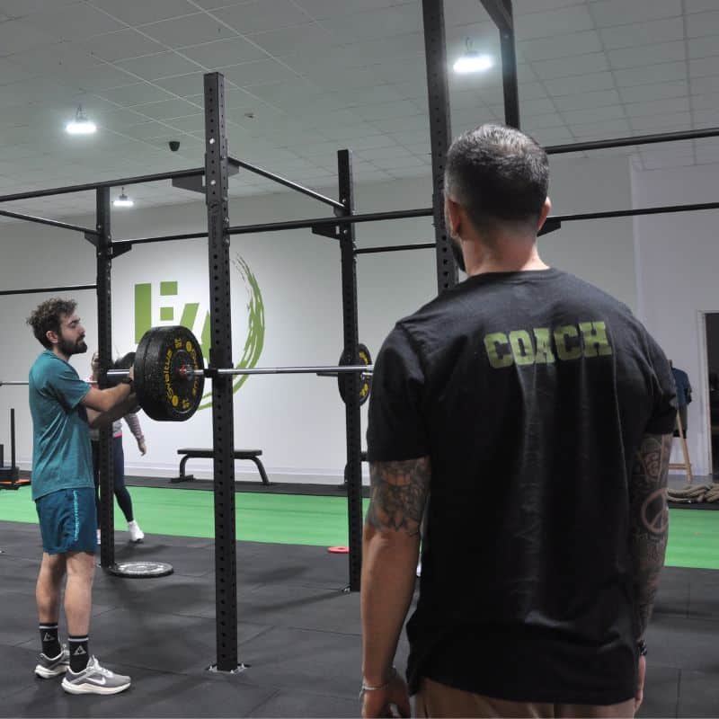Coaching de Musculation : Entraînement Guidé en Salle de Gym Un coach de sport supervisant un homme lors d'une séance de musculation avec barre chargée en salle de gym.