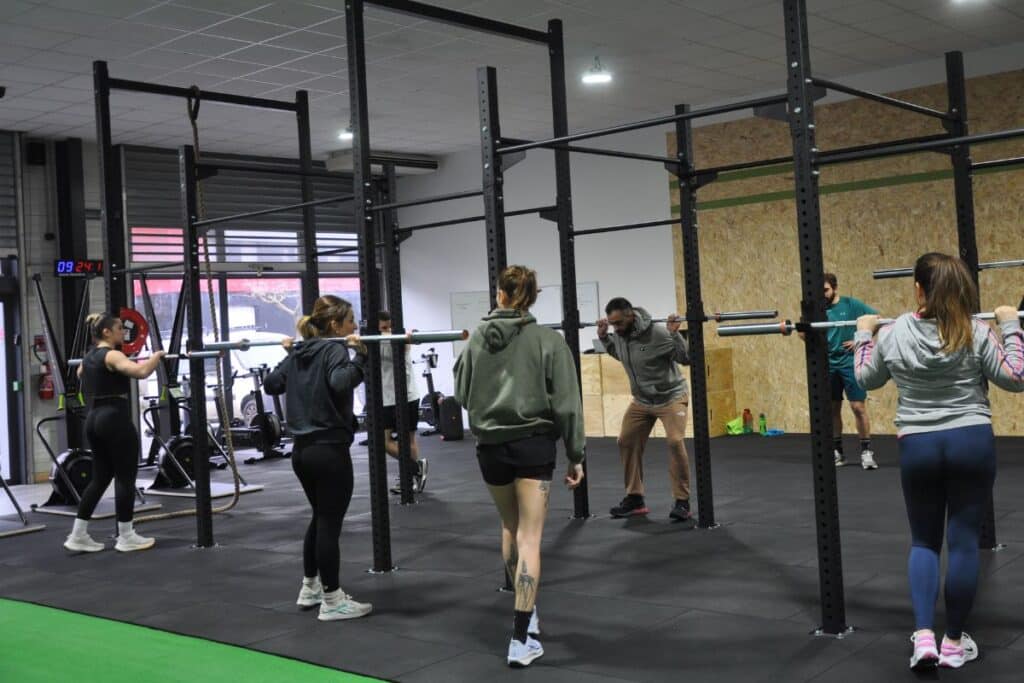 Entraînement de Squat Collectif en Box de CrossFit Groupe en pleine séance de squats avec barres dans une box de CrossFit. Horloge numérique affichant 09:24:1.