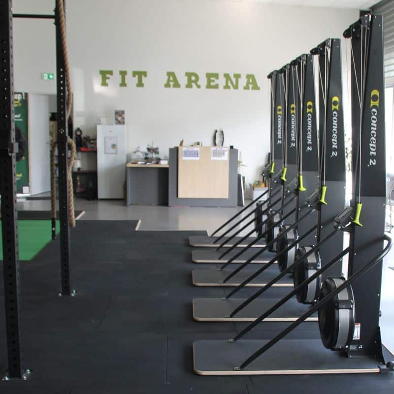 Salle de Sport Fit Arena : équipements Concept2 SkiErg pro Salle Fit Arena avec Concept2 SkiErg alignés sur sol sportif noir et zone d'accueil en arrière-plan.