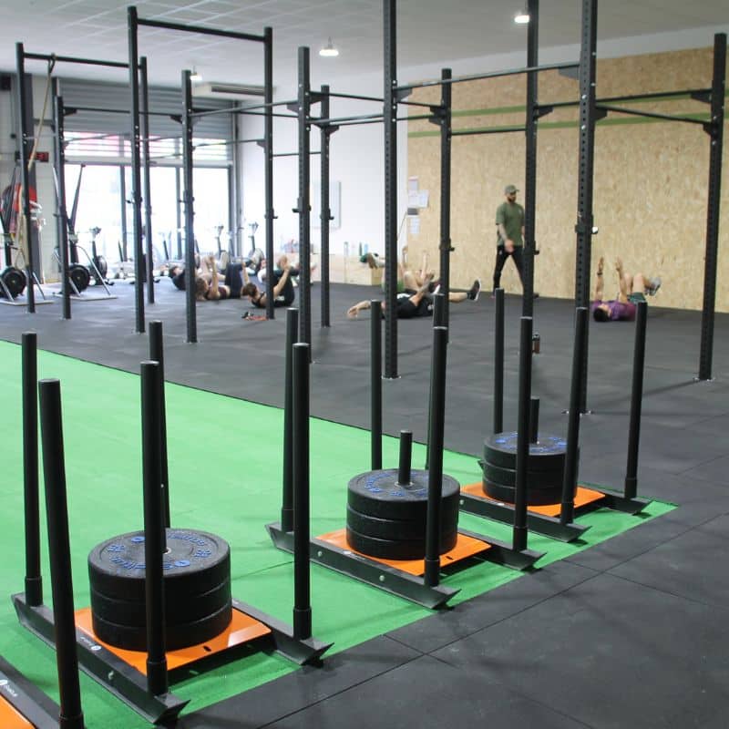 Traîneau de Puissance CrossFit : Séance d'Entraînement Traîneaux de puissance chargés sur gazon synthétique lors d'un entraînement collectif dans une salle de CrossFit.